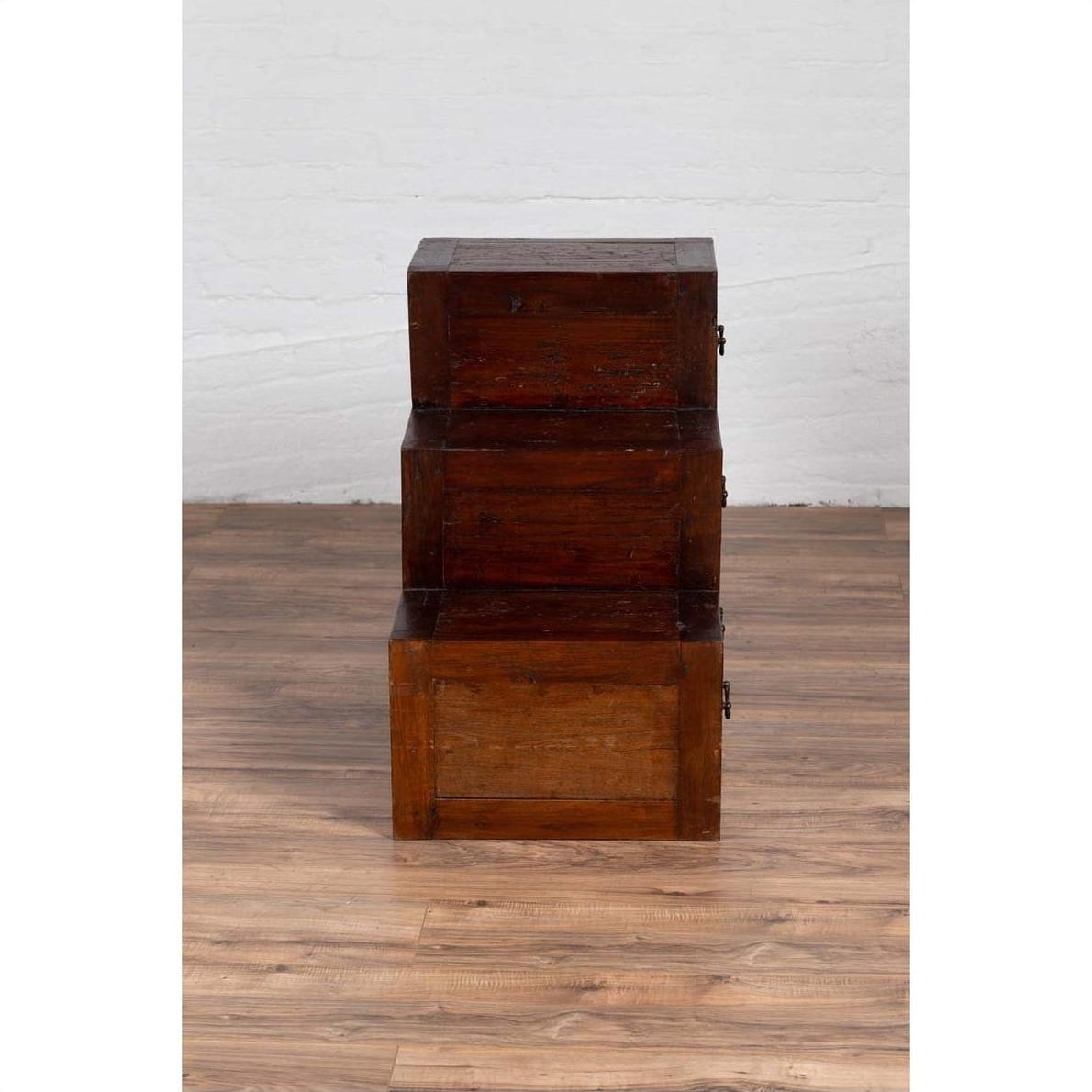 Brown wood staircase tansu cabinet with four drawers, Japanese style, indoors on wooden floor by white brick wall.