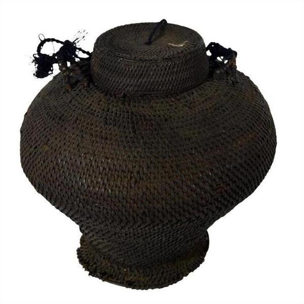 Brown woven basket made from natural fibers with wide body, narrow base, fitted lid, and braided handles.