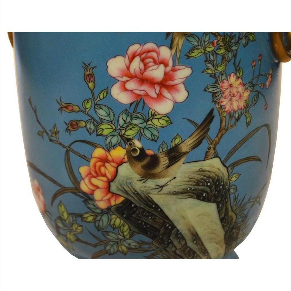 Close-up of a vintage porcelain vase with hand painted pink flowers and a bird on a rock, set against a blue background.