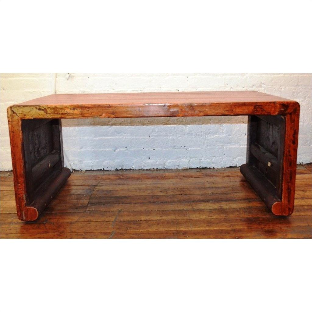 Light wood waterfall table with curved edges on wooden floor, white brick wall background.