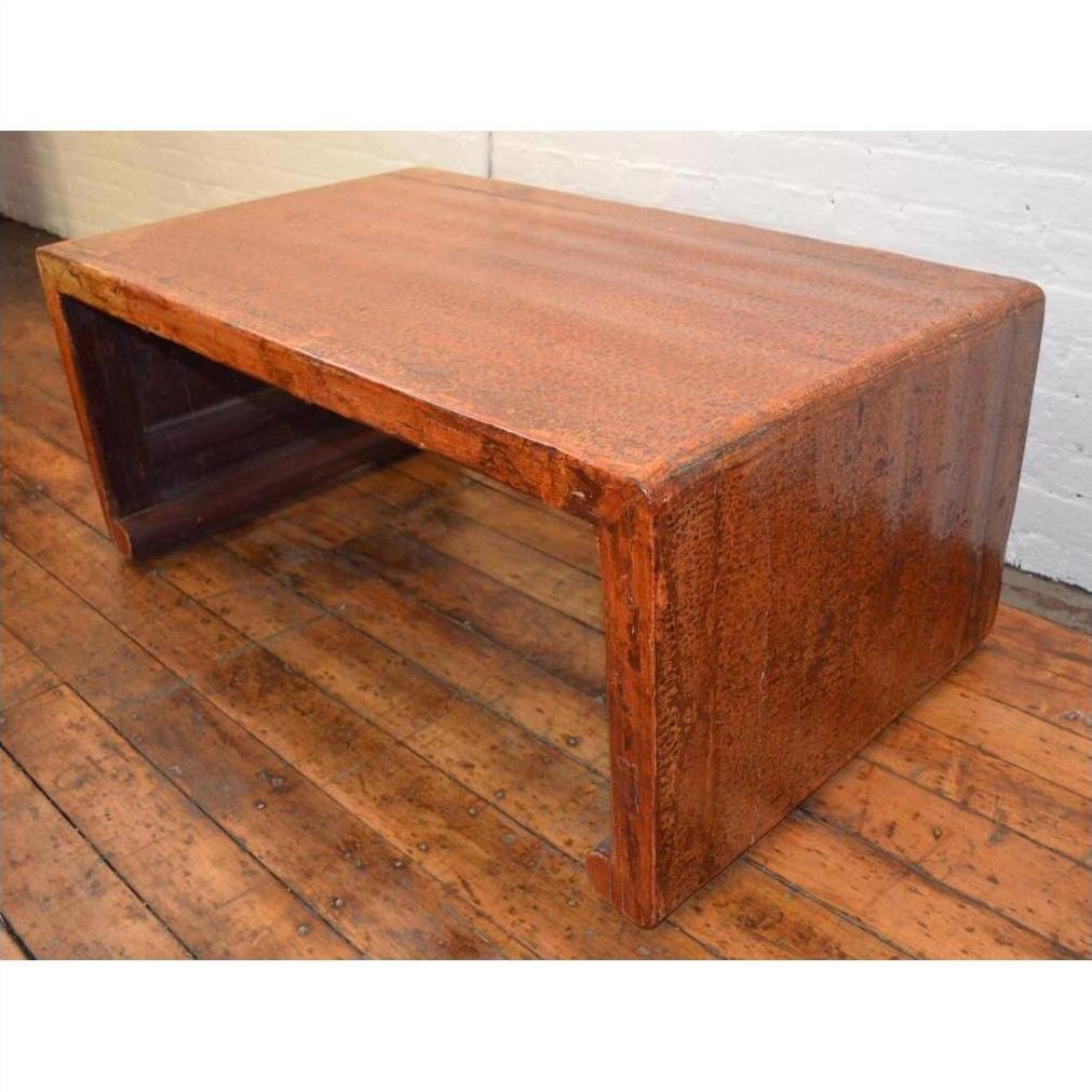 Brown wood waterfall coffee table with rustic Chinese antique style on wooden floor against white brick wall.