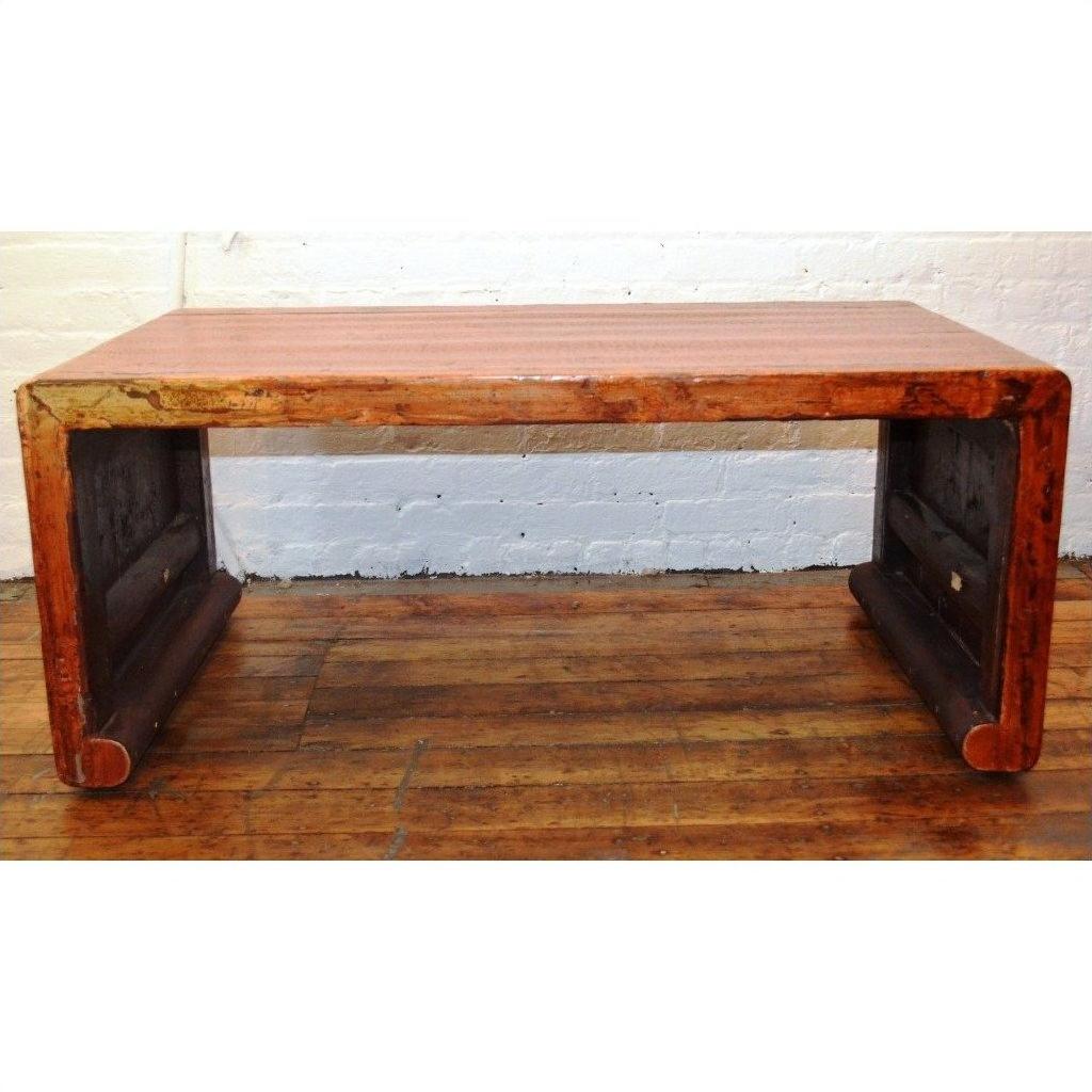 Light wood waterfall table with rounded edges on wooden floor, set against a white brick wall background.
