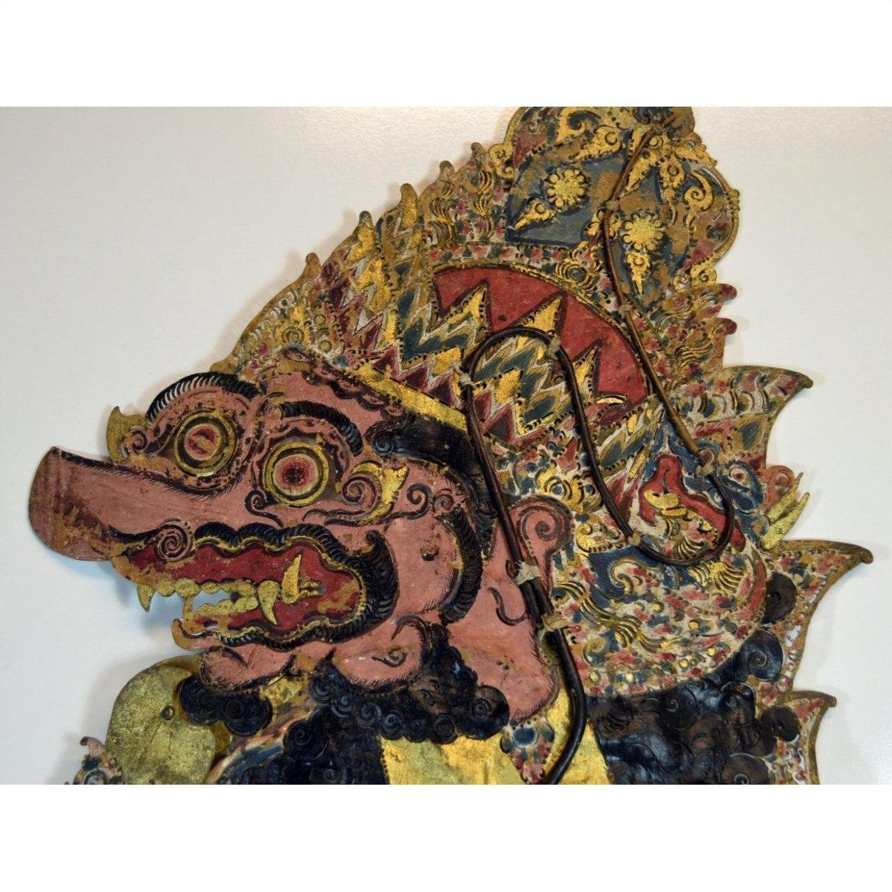 Brown cowhide Wayang Kulit Balinese shadow puppet with intricate patterns, bulging eyes, fierce expression, tall headdress.