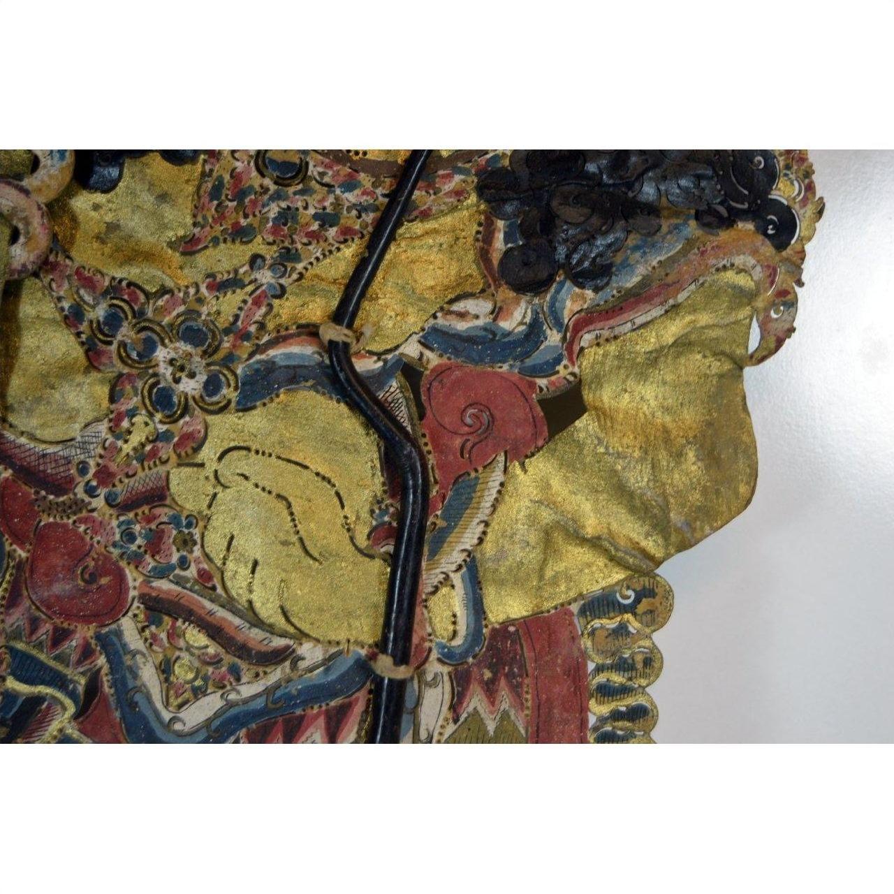 Close-up of yellow-hand Wayang Kulit shadow puppet made from Balinese cowhide, holding black stick on white background.