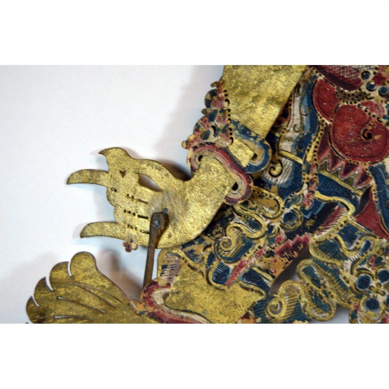 Close-up of gold-patterned Balinese Wayang Kulit cowhide shadow puppet hand with ornate detailing.