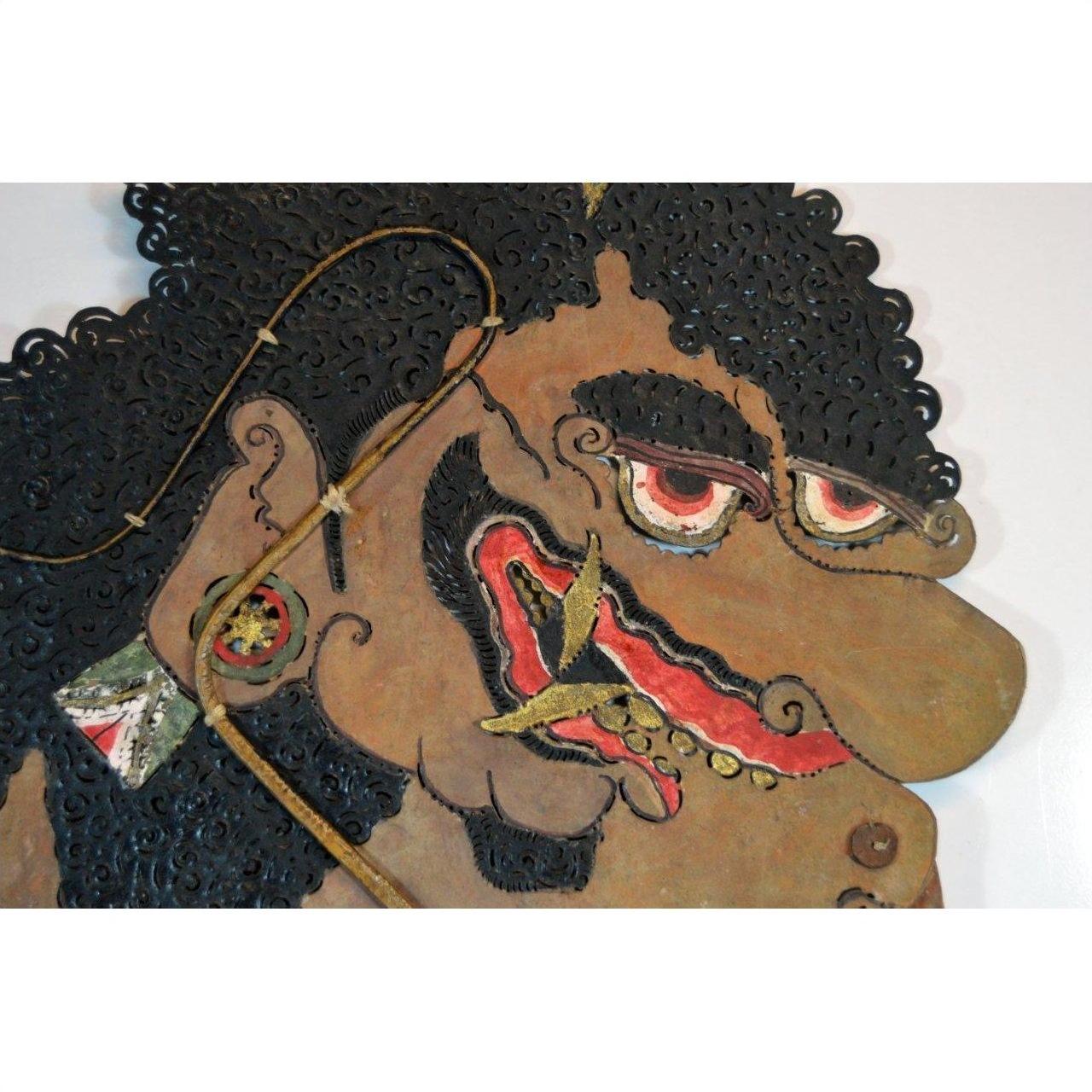 Close-up of an antique brown cowhide Wayang Kulit Balinese shadow puppet with curly hair and bold facial features.