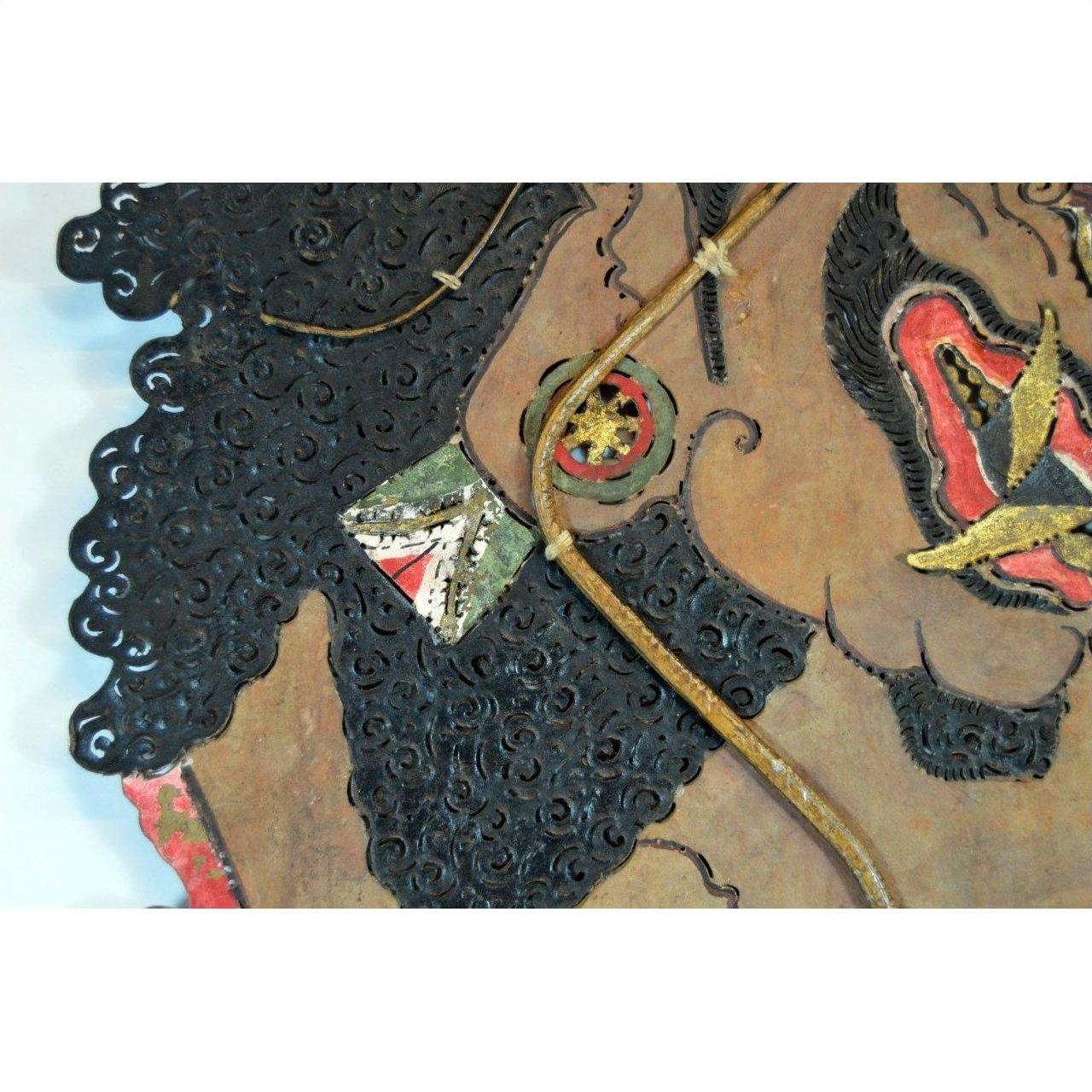 Close-up of antique Balinese Wayang Kulit shadow puppet with textured hair and detailed features, made from cowhide.