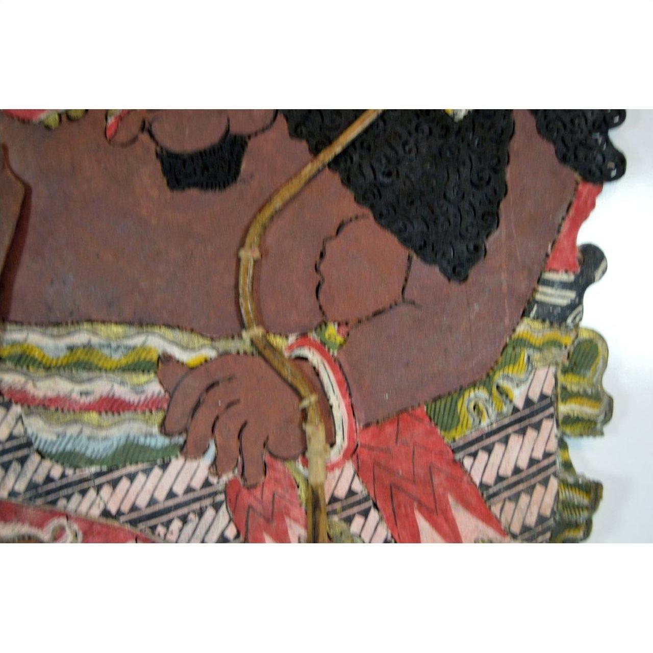 Close-up of brown cowhide arm and hand of Balinese Wayang Kulit shadow puppet with patterned garment.