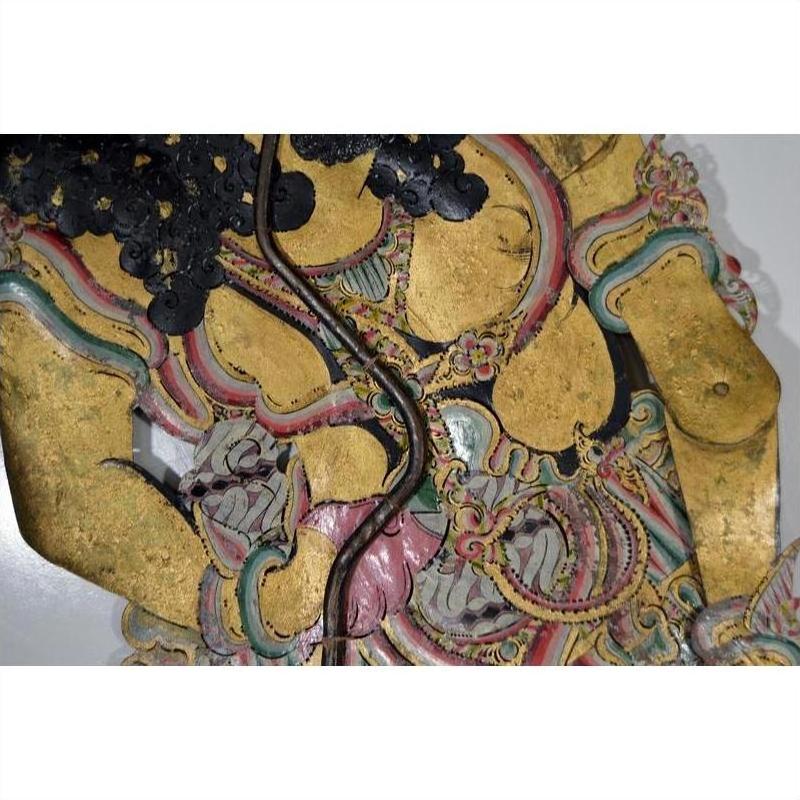 Close-up of gold-painted cowhide Wayang Kulit Balinese shadow puppet with detailed floral and intricate patterns.