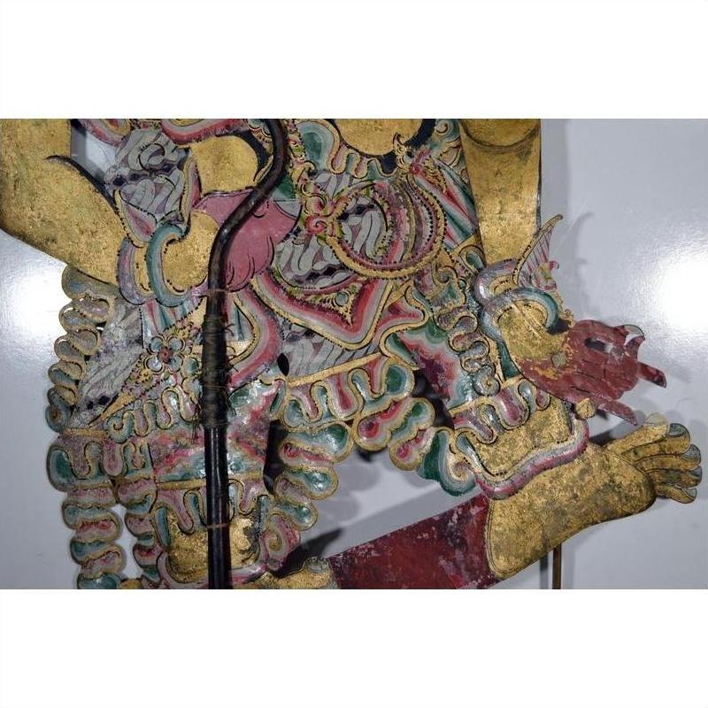 Balinese cowhide wayang kulit shadow puppet with ornate patterns and dragon-shaped foot on white background.