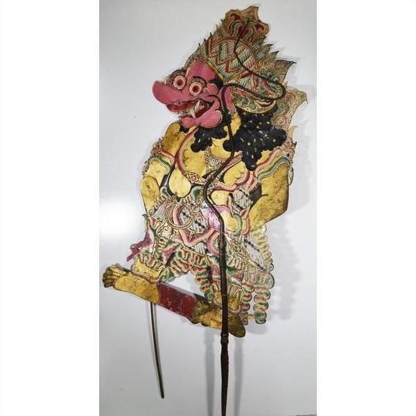 Close-up of ornate Wayang Kulit Balinese shadow puppet made from cowhide, holding two sticks against white background.