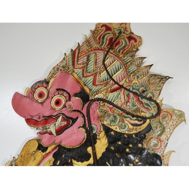 Pink cowhide Wayang Kulit shadow puppet with bulging eyes and ornate headdress on white background.