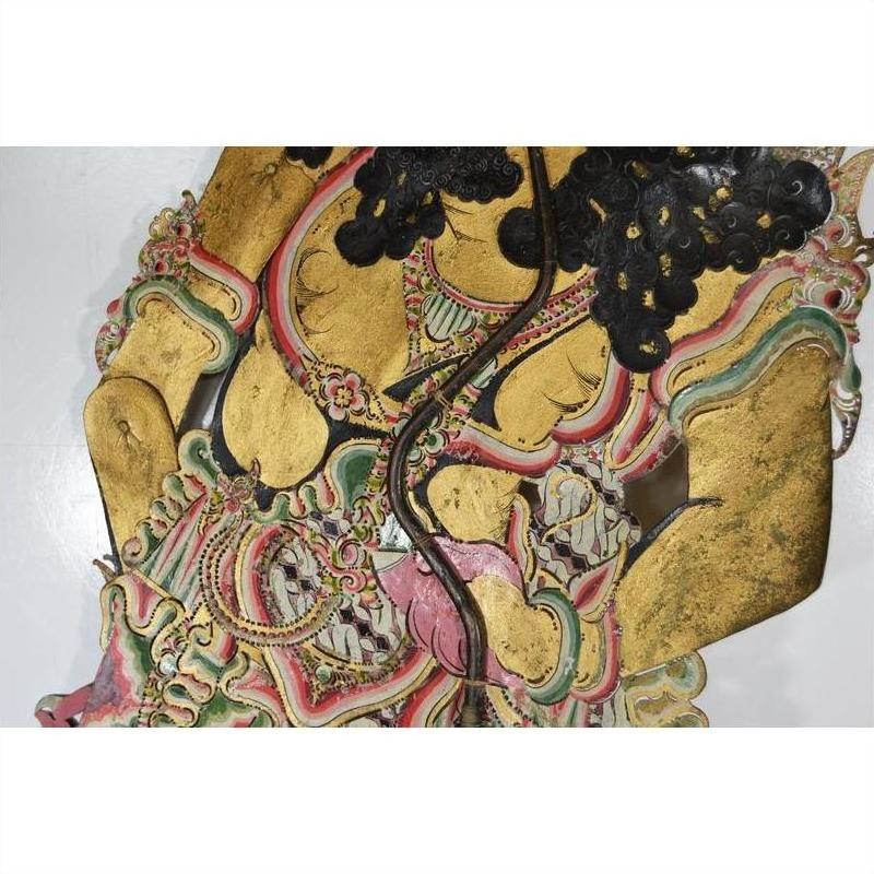 Gold-accented cowhide Wayang Kulit shadow puppet with intricate patterns, elaborate costume, close-up.