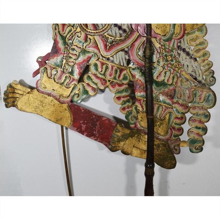 Gold and brown cowhide wayang kulit shadow puppet with ornate patterns on a white background.