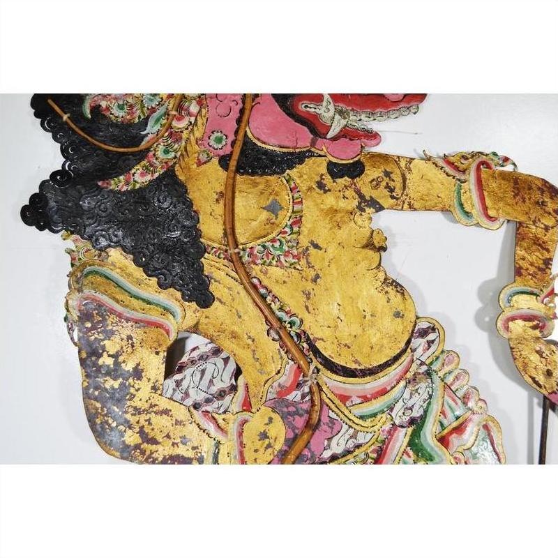 Close-up of gold, pink, and green Wayang Kulit shadow puppet made from Balinese cowhide on white background.