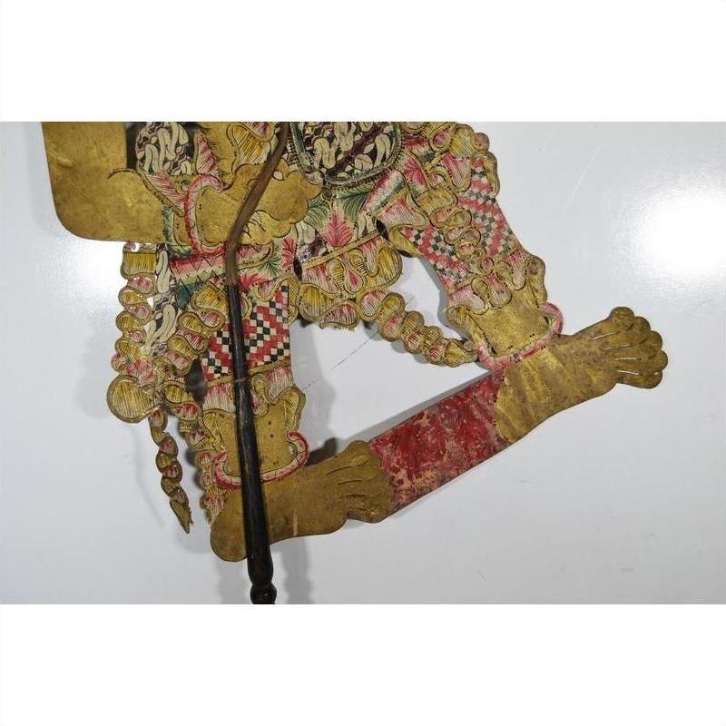 Colorful cowhide Wayang Kulit Balinese shadow puppet with bare feet on a plain white background.
