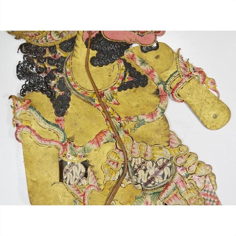 Close-up of a vibrant Balinese Wayang Kulit shadow puppet made from cowhide with intricate patterns and curly black hair.