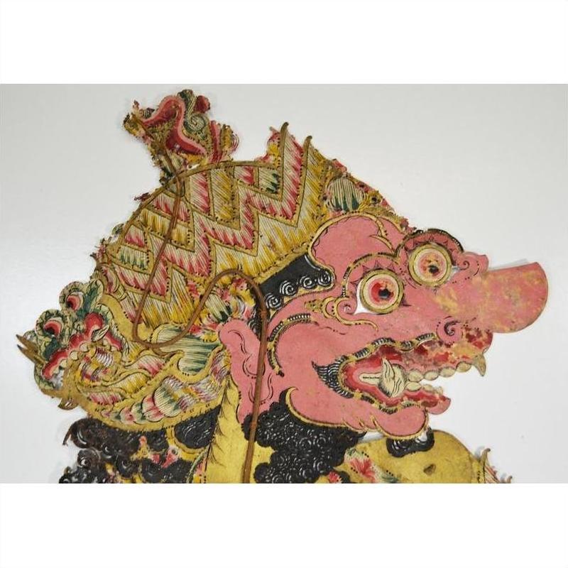 Close-up of pink-faced Balinese cowhide Wayang Kulit shadow puppet with large nose, fangs, Javanese headdress.