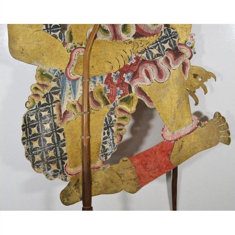 Close-up of gold, red, and blue Wayang Kulit Balinese shadow puppet made from cowhide on a white background.
