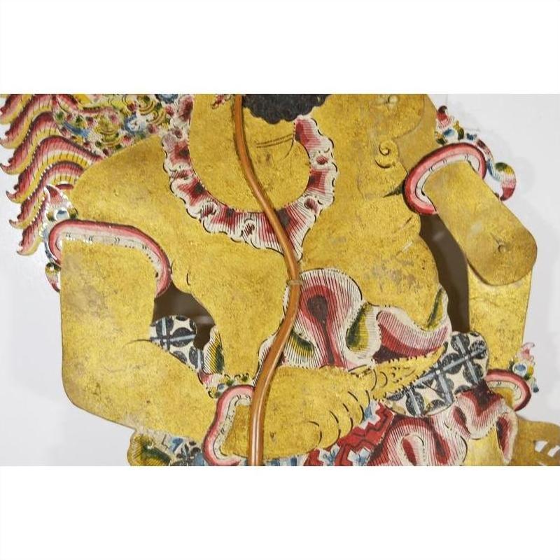 Close-up of gold, red, and black Wayang Kulit shadow puppet made from Balinese cowhide with ornate patterns.