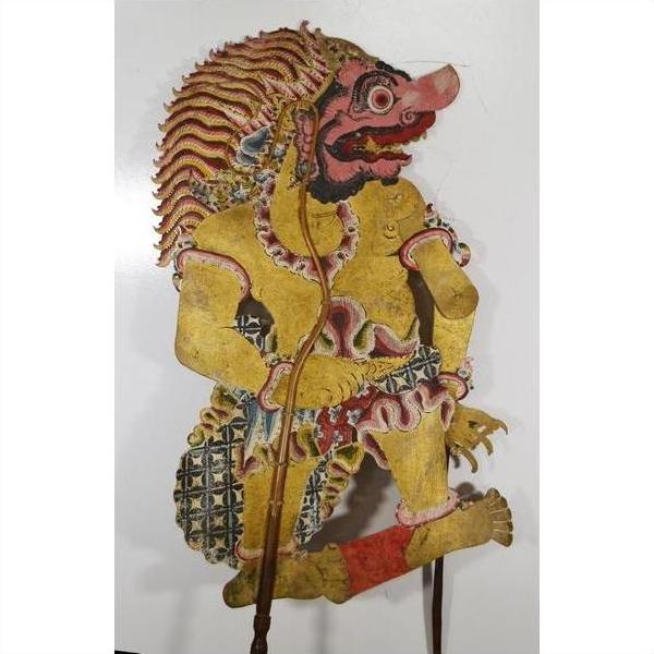 Yellow cowhide Wayang Kulit Balinese shadow puppet with red face and ornate headdress, close-up view.