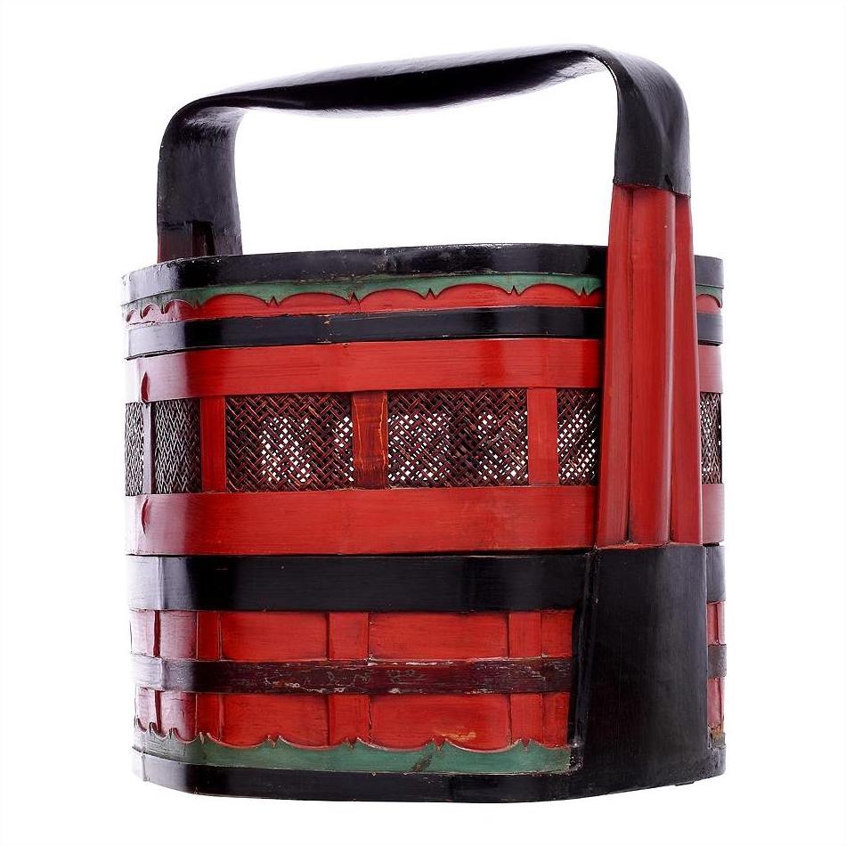Close-up of a red and black wedding basket with green accents, large handle, and decorative cut-out side patterns.
