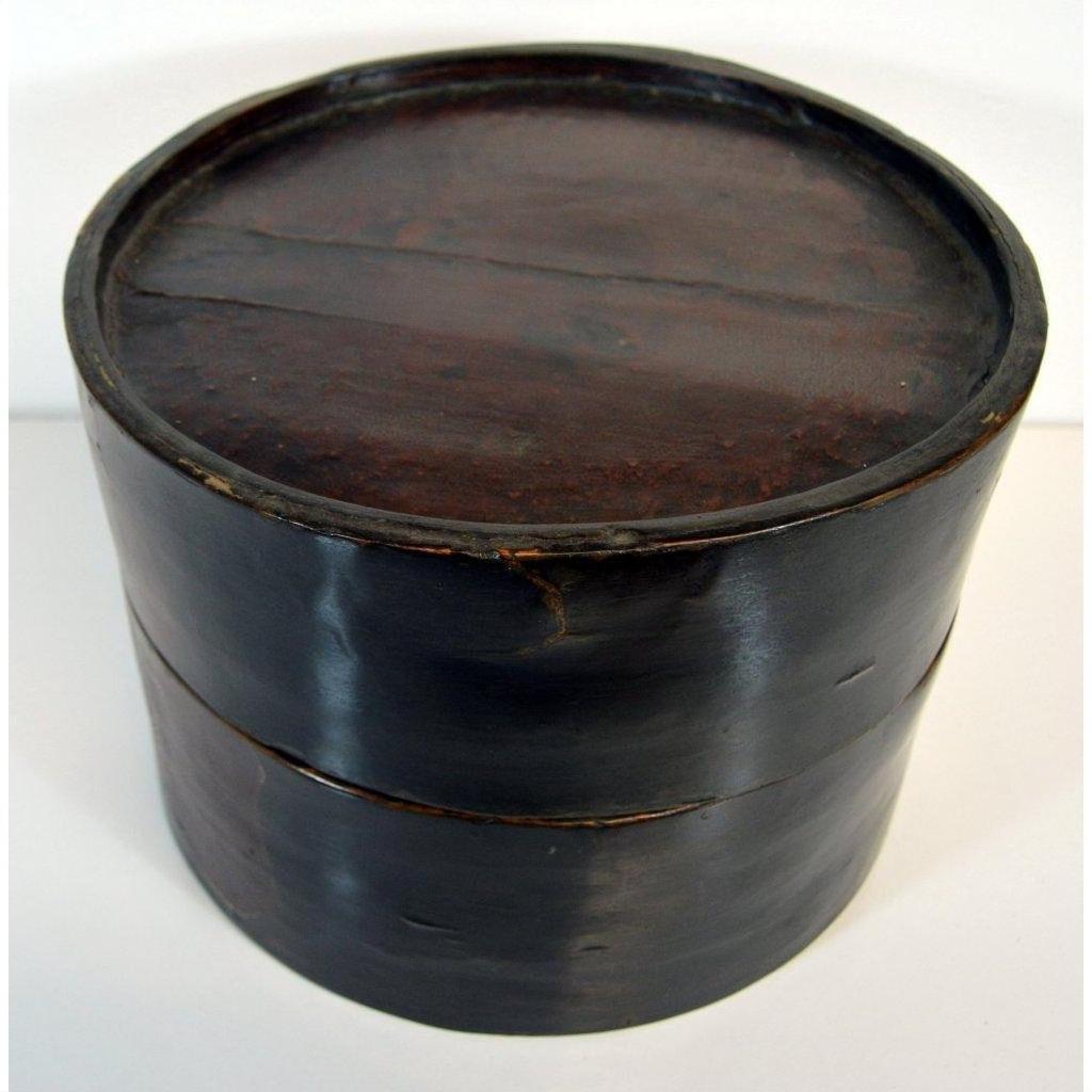 Close-up of round dark brown wooden hat box with Chinese design, lid on, light and dark wood, visible scratches.
