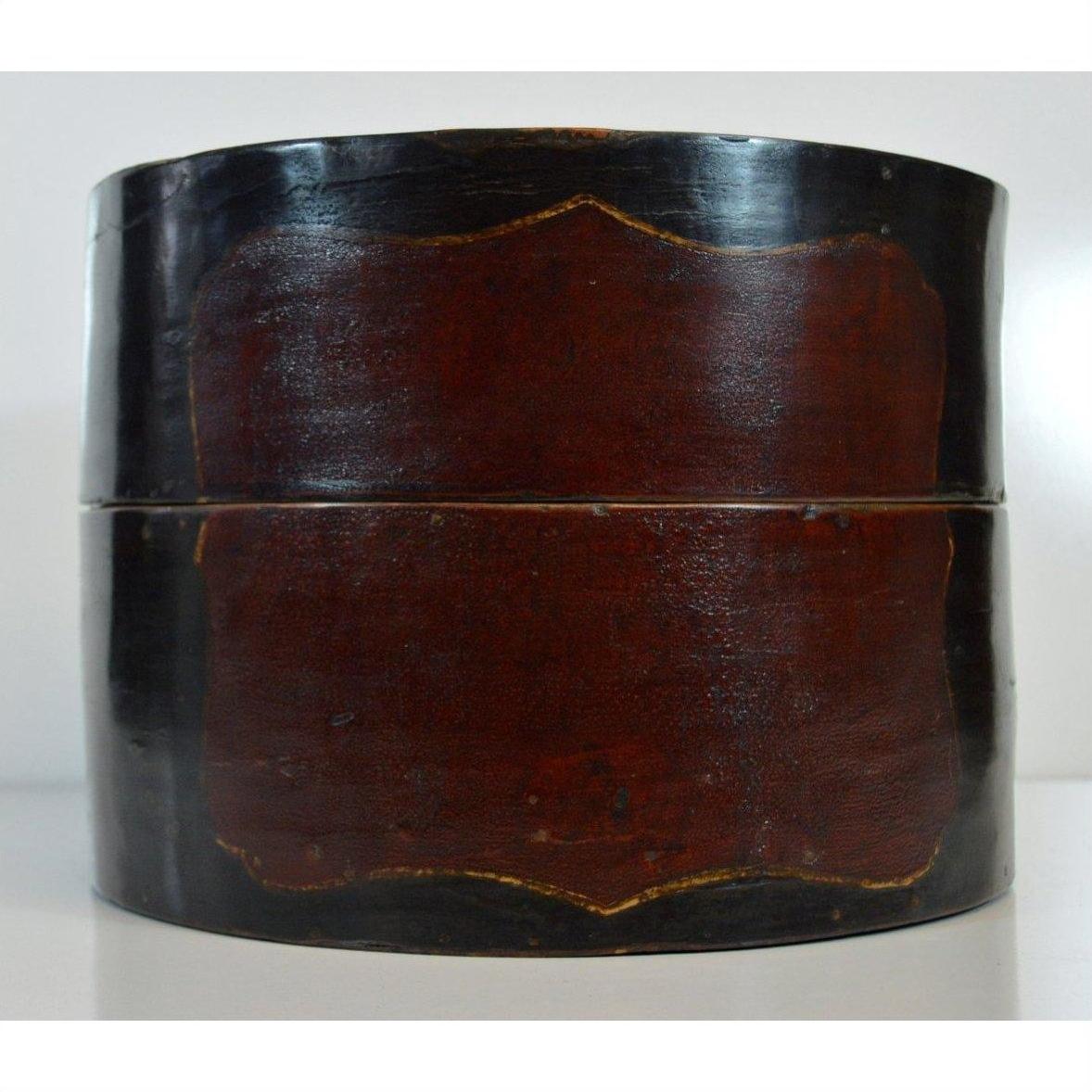 Close-up of round vintage hat box in dark wood with a central red rectangular panel, isolated on white background.