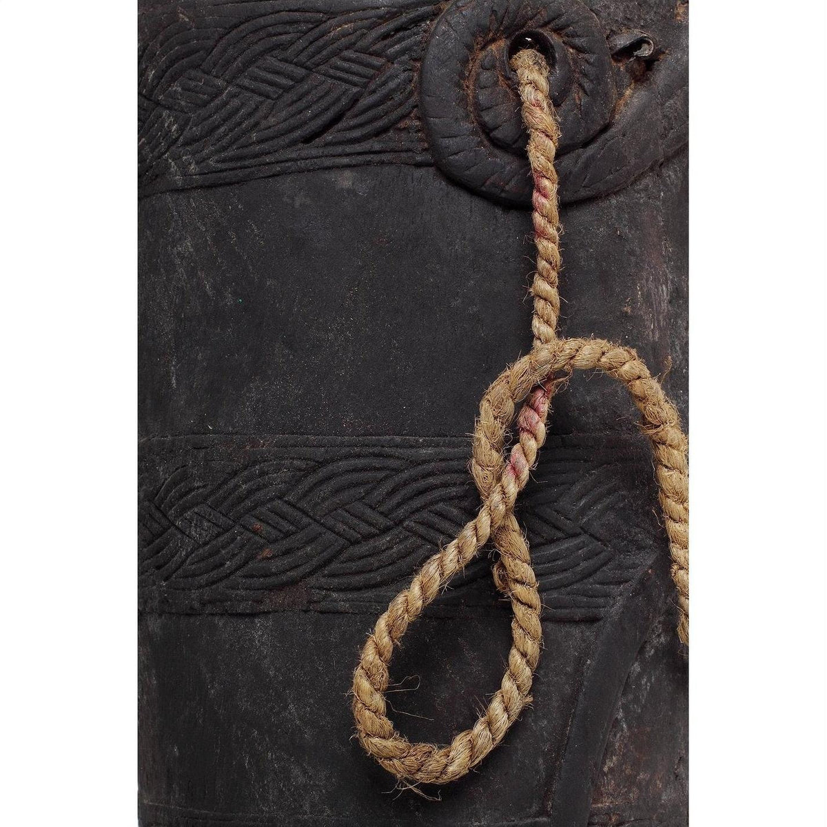 Close-up of a braided rope looped through a decorative brown wooden Indian pitcher on a plain background.