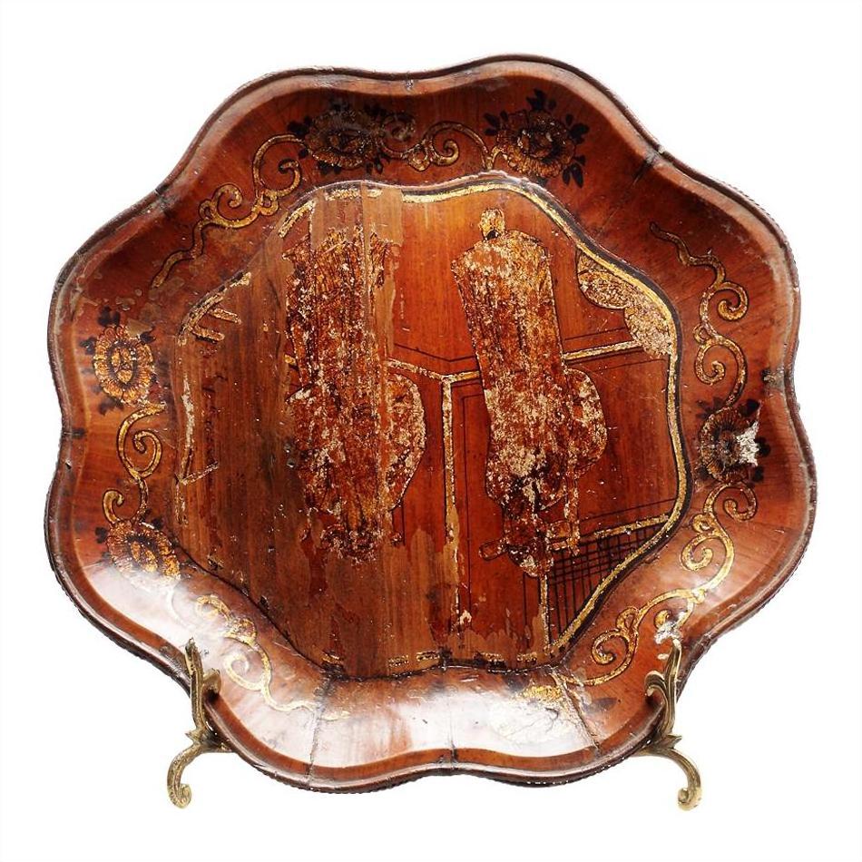 Brown wooden platter with scalloped edges, gold floral accents, gilt design, and a faded central motif on a stand.