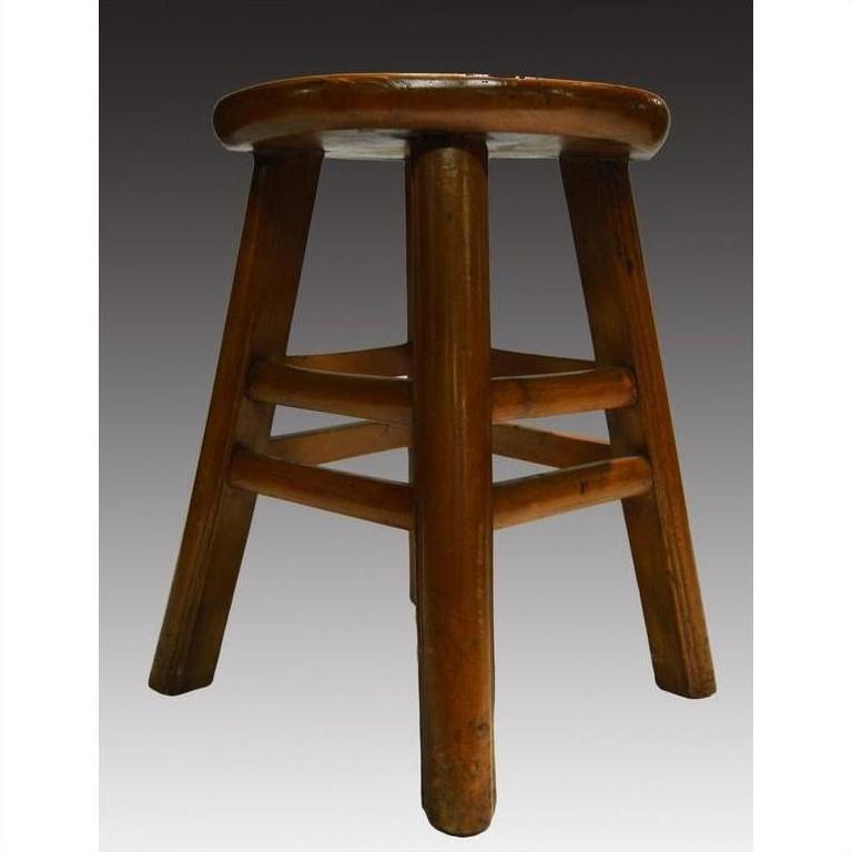 Brown wooden antique Indonesian stool with four legs and round seat on a gradient gray background.