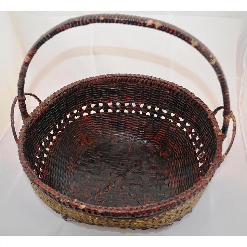 Dark brown woven bamboo offering basket with sturdy handle, close-up against a plain light background.