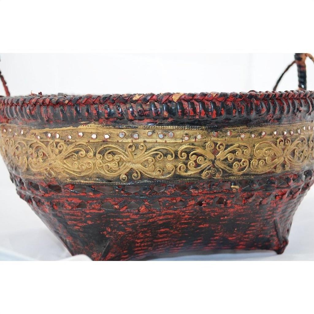 Close-up of red and gold woven bamboo offering basket with gilt décor, woven rim, and handles.