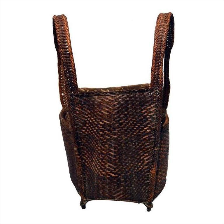 Natural rattan basket with tall looped handles and rounded rectangular shape, top view.