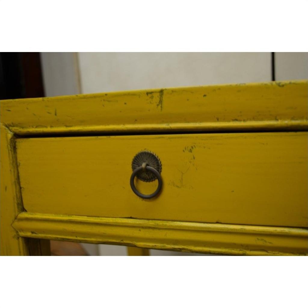 Close-up of yellow wood side table drawer with distressed finish and round metal ring pull handle at center.