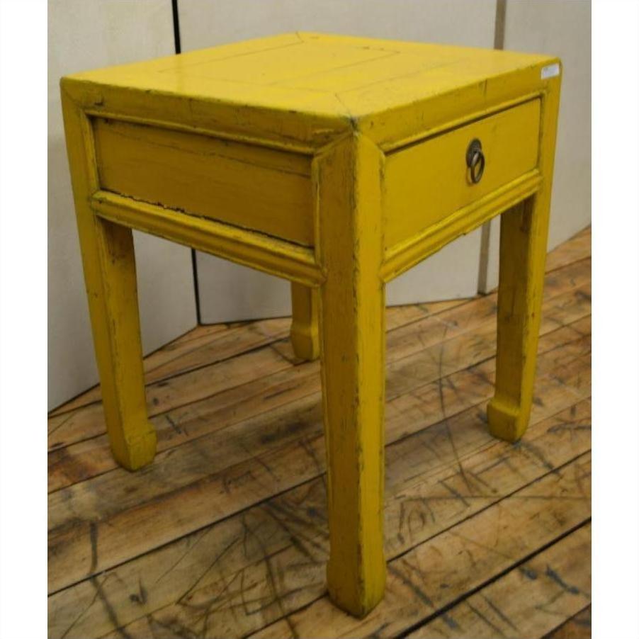 Yellow wood side table with single drawer and horse hoof feet, on wooden floor indoors.