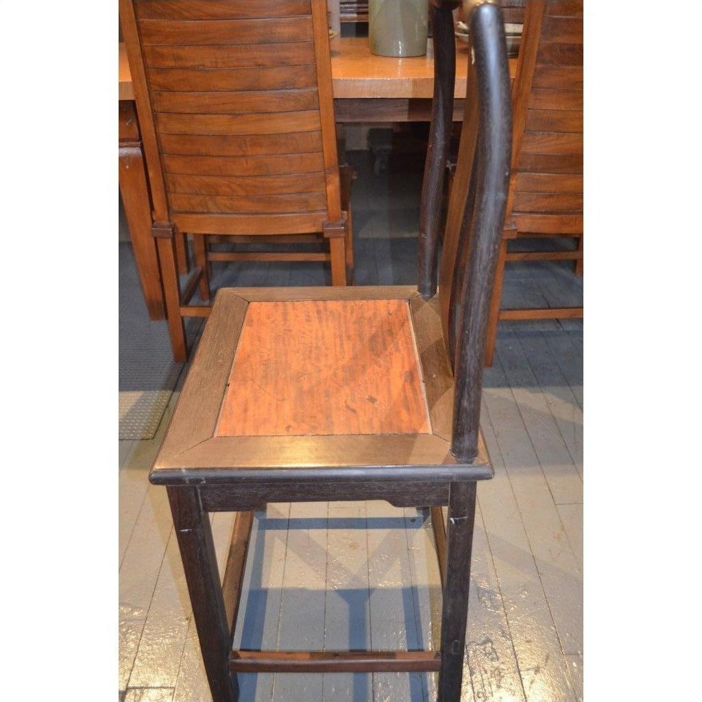 Dark brown wood Yoke Back Chair with high back and burl wood seat on wooden floor near matching table and chairs.